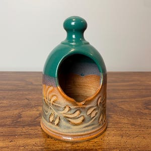 May include: A ceramic salt cellar with a green top and a brown base with a leaf design. The salt cellar has a round opening on the top.