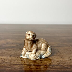 May include: A brown ceramic figurine of an otter sitting on a rock. The figurine is part of a collection of animal figurines.