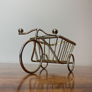 May include: A silver metal decorative tricycle shaped wire basket. The basket has a rectangular shape with a wire frame and a rounded top.