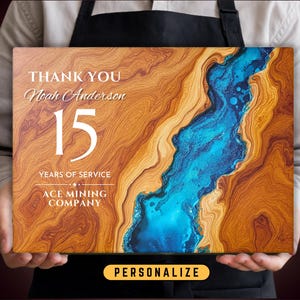 May include: A wooden plaque with a blue and brown abstract design. The plaque says "Thank You Noah Anderson 15 Years of Service Ace Mining Company".