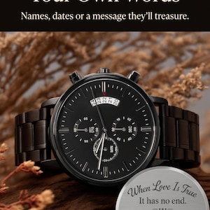 May include: A black chronograph wristwatch with a metal link band and a round face featuring three sub-dials. Beside it sits a circular silver metal plaque engraved with the text: When Love Is True, It has no end. Happy Anniversary.