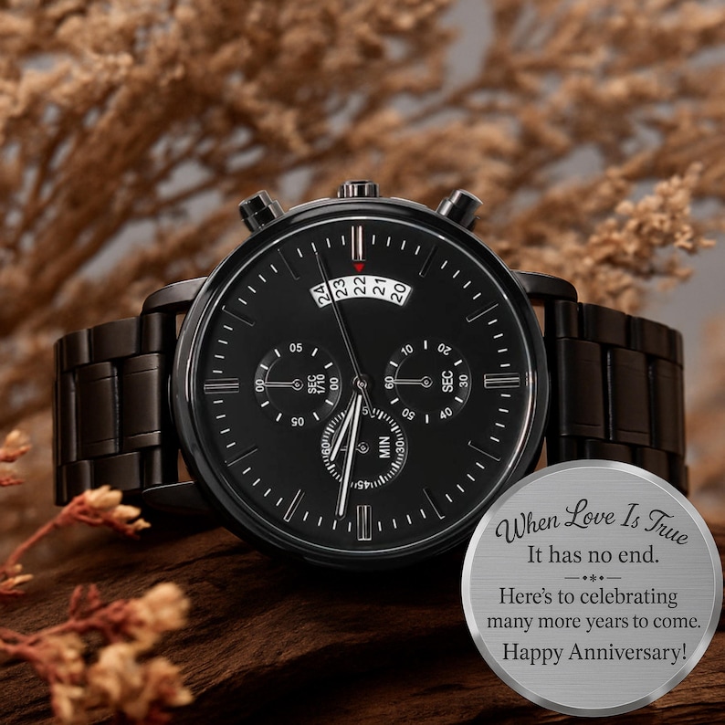 May include: A black chronograph wristwatch with a metal link band and a black dial featuring three sub-dials and a date window. Beside the watch is a round silver-toned metal disc engraved with the text: When Love Is True It has no end. Here's to celebrating many more years to come. Happy Anniversary!