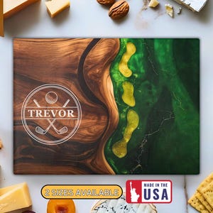 Puede incluir: Tabla de cortar rectangular de madera con dise&ntilde;o de campo de golf. La tabla presenta un patr&oacute;n de vetas de madera marr&oacute;n a la izquierda y un dise&ntilde;o de resina epoxi verde y amarilla a la derecha. La tabla tiene el nombre "TREVOR" en un c&iacute;rculo blanco.