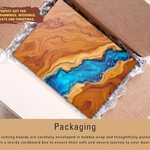 May include: A wooden cutting board with a blue resin inlay. The board is packaged in a cardboard box with bubble wrap for protection. The text "PERFECT GIFT FOR HOUSEWARMINGS, WEDDINGS, BIRTHDAYS AND CHRISTMAS." is printed on the box.
