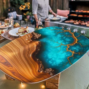 May include: A large, oval serving tray made of wood and resin. The tray has a natural wood finish on one side and a blue and gold resin finish on the other side. The resin has a swirling pattern that resembles water.
