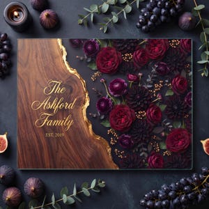 May include: A rectangular glass cutting board featuring a dark wood grain section on the left with a gold-colored edge and the text The Ashford Family EST. 2019. The right side displays a dark floral arrangement of deep red and purple roses.