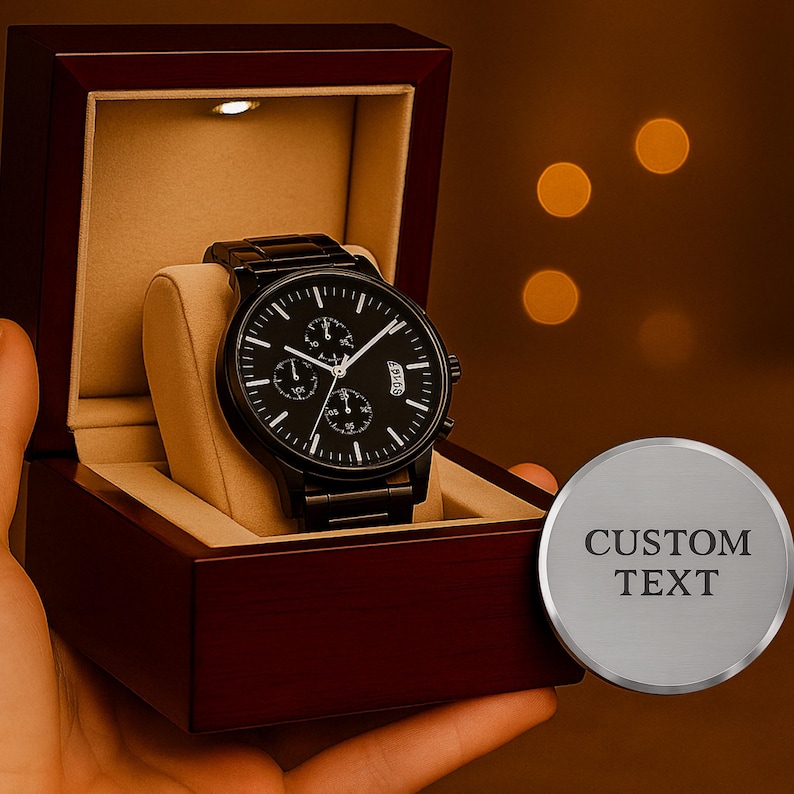 May include: A black analog wristwatch with a round face, three sub-dials, and a date window, displayed inside a dark mahogany-colored wooden box with a beige interior and a small LED light. A circular silver-toned metal plaque reads CUSTOM TEXT.