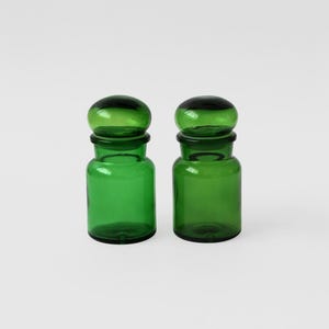 May include: Two green glass bottles with round tops. The bottles are opaque and have a smooth, shiny finish.