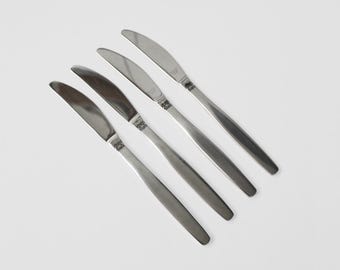 May include: Four silver dinner knives with a simple design. The knives are arranged in a row, with the handles pointing to the right.