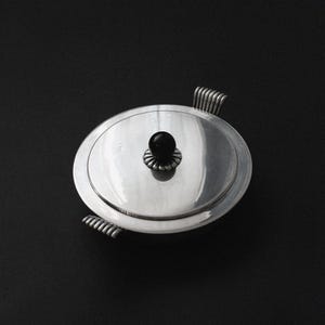 Puede incluir: Un plato de servir de plata con un pomo negro en la tapa y dos asas a los lados.