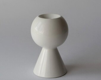 May include: A white ceramic candle holder with a spherical top and a conical base. The glossy finish reflects light, highlighting the smooth curves of the modern design. This decorative piece is suitable for various home decor styles.