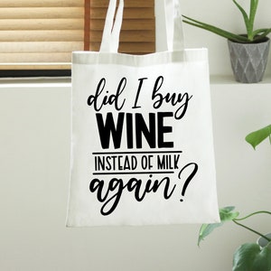 May include: A white tote bag with black text that reads "did I buy WINE INSTEAD OF MILK again?". The bag has long handles and is held up by a person. The background includes a window and plants.