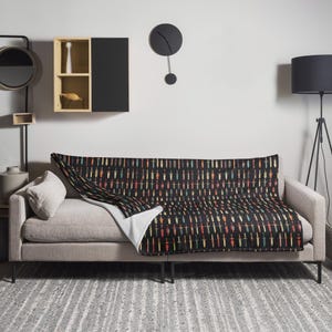 May include: A black couch with a throw blanket featuring a repeating pattern of colorful swords on a black background.