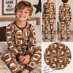 May include: A two-piece pajama set featuring a long-sleeve crew neck top and matching pants with an all-over brown and white football print. The garment has dark brown ribbed cuffs at the wrists and ankles, with a repeating pattern of footballs.
