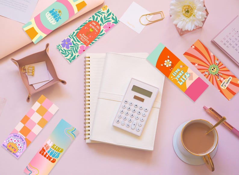 Puede incluir: Una vista cenital de una superficie rosa con varios marcadores de colores, un cuaderno, una calculadora, una taza de caf&eacute; y un calendario. Los marcadores presentan diferentes dise&ntilde;os y citas inspiradoras, como "Trabaja duro, s&eacute; amable", "Eres hermosa, por dentro y por fuera", "Vive tu vida" y "S&eacute; amable con tu mente".