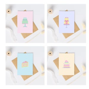 Op de afbeelding: Vier verschillende wenskaarten met illustraties van taarten. De kaarten liggen op een witte achtergrond met bruine enveloppen en wat decoratieve items.