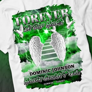 May include: White t-shirt with a green and white graphic design. The graphic features a pair of angel wings, a stairway to heaven, and the text "FOREVER In Our Hearts DOMINIC JOHNSON Heaven Couldn't Wait SUNRISE - SUNSET".