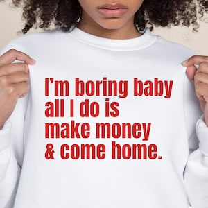 Puede incluir: Sudadera blanca con texto rojo que dice "Soy un bebé aburrido, todo lo que hago es ganar dinero y volver a casa."