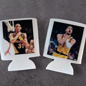 May include: Two white can coolers, each featuring a basketball player in a yellow and black uniform. The players are depicted with their hands around their necks. The can coolers have a computer monitor shape.