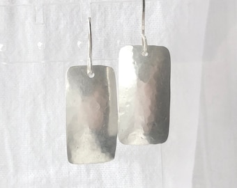 May include: A pair of silver earrings with a hammered rectangular shape. The earrings have a simple design and are a classic style.