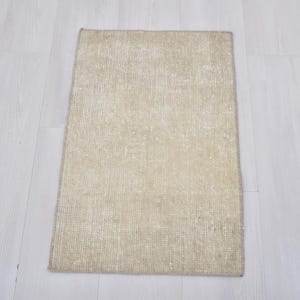 May include: A rectangular area rug featuring a woven texture in a neutral beige color palette. The rug displays a subtle, faded pattern across its surface with a consistent weave throughout, finished with a simple bound edge on all four sides.