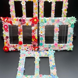 May include: Five rectangular light switch plates decorated with various small plastic flowers, butterflies, and beads. Two plates feature warm red, orange, and yellow tones, while three plates display cool pastel shades of blue, pink, and green.