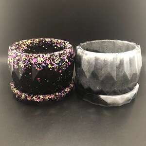 May include: Two geometric concrete planters, one black with colorful iridescent glitter and one gray. Both planters have a matching saucer.