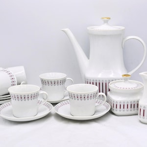 May include: A white porcelain tea set with a red and grey pattern. The set includes a coffee pot, sugar bowl, creamer, cups, and saucers. The coffee pot and sugar bowl have gold detailing. A classic tea set.