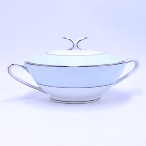May include: A covered sugar bowl with a light blue band and white base. The bowl has two handles and a silver trim. The lid has a decorative handle. The bowl has a floral pattern on the light blue band.