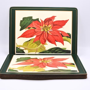 Op de afbeelding: Set van zes vierkante onderzetters met een poinsettia bloemmotief. Elke onderzetter toont een levendige rode poinsettia met groene bladeren tegen een crèmekleurige achtergrond, omlijst door een donkergroene rand. Perfect voor de feestdagen.