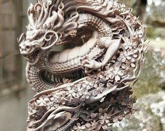 May include: A detailed, intricately carved dragon sculpture made of a light brown material. The dragon is curled around a tree trunk, with its head raised and its wings spread. The sculpture is set on a circular base.