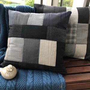 Könnte beinhalten: Zwei graue und schwarze Patchwork-Wurfkissen mit verschiedenen Texturen. Die Kissen liegen auf einer Holzoberfläche.