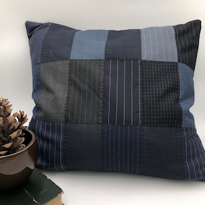 Könnte beinhalten: Ein blaues und graues Patchwork-Kissen mit quadratischem Muster. Das Kissen ist aus verschiedenen Stoffen mit unterschiedlichen Texturen gefertigt.