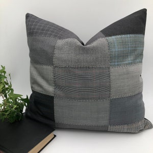 Peut inclure: Un oreiller patchwork gris et noir avec une variété de motifs différents. L'oreiller est fait de matériaux recyclés et a un aspect unique et fait main.
