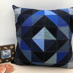 Peut inclure: Un coussin carré bleu et bleu marine avec un motif géométrique composé de différentes nuances de tissu bleu. Le coussin est fabriqué à partir de matériaux recyclés.