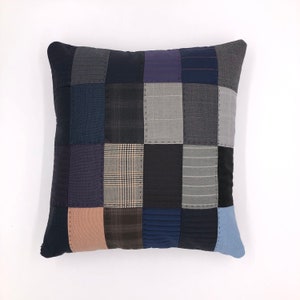 Peut inclure: Une housse de coussin en patchwork faite de différentes nuances de bleu, gris et marron. La housse de coussin est faite de matériaux recyclés et a un aspect unique et fait main.