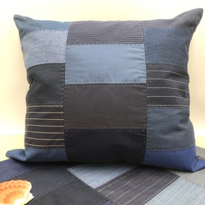 Puede incluir: Una almohada azul y negra de patchwork con un diseño cuadrado. La almohada está hecha de diferentes telas, incluyendo denim y tela a rayas.