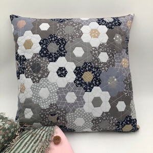 Puede incluir: Una almohada gris, blanca y azul con un diseño hexagonal. La almohada está hecha de tela y tiene una textura suave y cómoda.