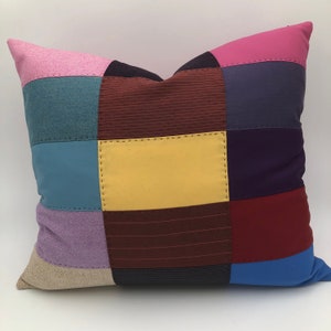 Könnte beinhalten: Ein Patchwork-Kissen mit verschiedenen Farben und Texturen, darunter Rosa, Blau, Gelb, Rot und Lila. Das Kissen ist aus verschiedenen Stoffen gefertigt, darunter Tweed, Cord und Denim.