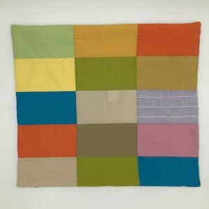 Puede incluir: Una almohada de patchwork con una variedad de colores y texturas, incluyendo verde, amarillo, naranja, azul, marrón y morado.
