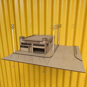 May include: A laser-cut wooden model of a single-story commercial building with a flat roof, a garage bay, and a storefront. The model includes a base with parking lines, three white utility poles, and the text "TONY'S" etched above the entrance.