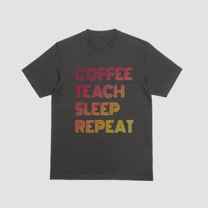 Puede incluir: Una camiseta gris oscuro con un estampado gráfico del texto "COFFEE TEACH SLEEP REPEAT" en un degradado de rojo, naranja y amarillo.