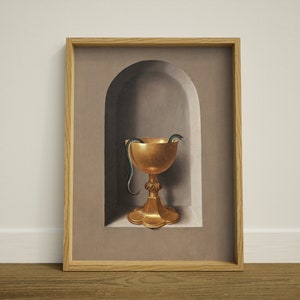 May include: A framed print featuring a gold chalice with a snake inside, set in a recessed alcove. The chalice has an ornate base and a wide bowl. The snake is dark green and black. The frame is made of light-colored wood.