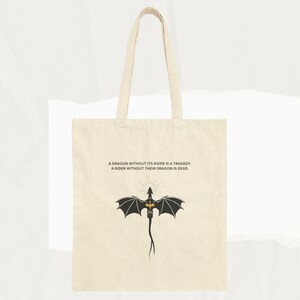 May include: A beige tote bag with black handles and a black silhouette of a dragon with gold accents. The bag has the text "A dragon without its rider is a tragedy. A rider without their dragon is dead."