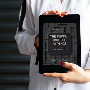 May include: A black tablet displaying the cover of a book titled "The Puppet and the Strings." The cover features a dark gray background with a textured pattern and the book's title in white text. The author's name is also visible.