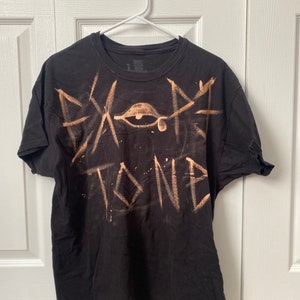May include: Black t-shirt with a bleach-splattered design featuring an eye with a tear and the word "STONE" in large, stylized letters.