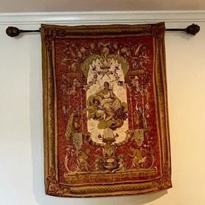 May include: A tapestry with a red background and gold trim. The tapestry features a central image of a woman holding a lyre, surrounded by intricate floral and geometric designs.