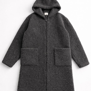 May include: A charcoal gray long-length coat made of textured fleece material. This garment features a hood, long sleeves, a full-length front zipper closure, and two large square patch pockets positioned on the front lower section of the coat.