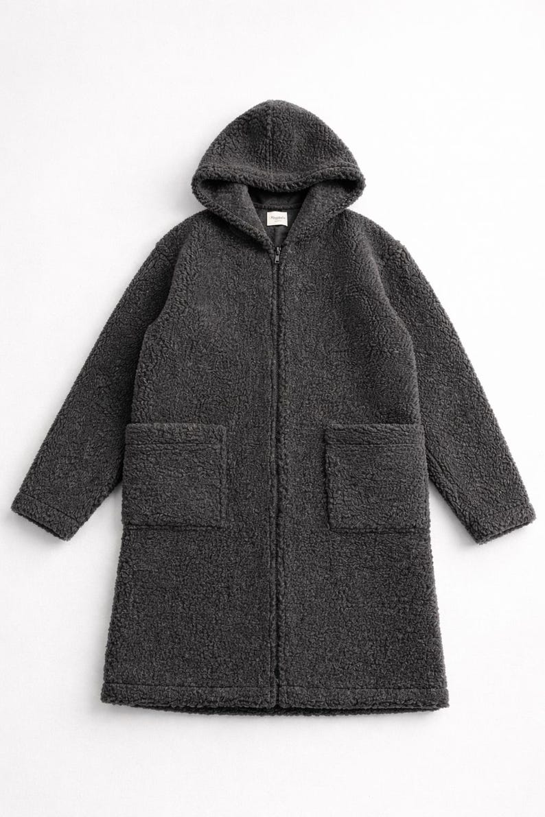 May include: A charcoal gray long-length coat made of textured fleece material. This garment features a hood, long sleeves, a full-length front zipper closure, and two large square patch pockets positioned on the front lower section of the coat.