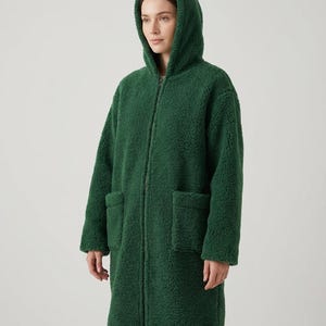 May include: A forest green zip-up coat made of a textured, curly fleece material. This long-sleeved garment features a hood, a full-length front zipper closure, and two large, square patch pockets positioned on the front of the coat.